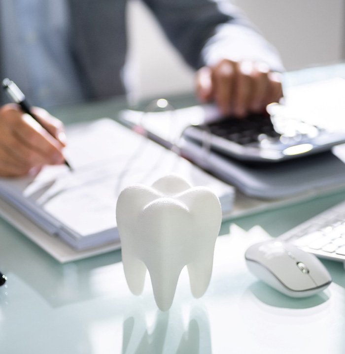 A 3D model tooth in front of a businessperson calculating a bill