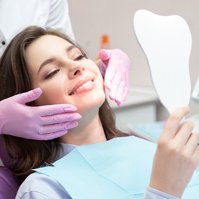 A woman admiring her smile with a hand mirror after treatment