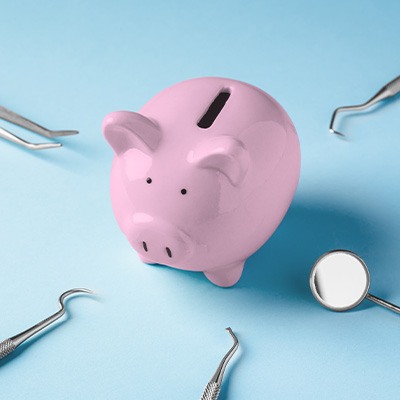 A piggy bank surrounded by dental instruments on a blue background