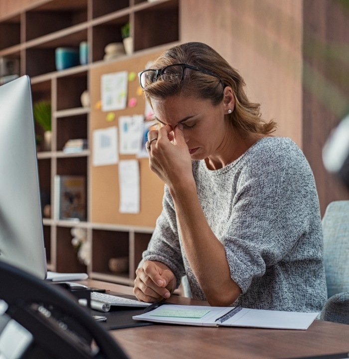 Tired woman at desk pinching the bridge of her nose